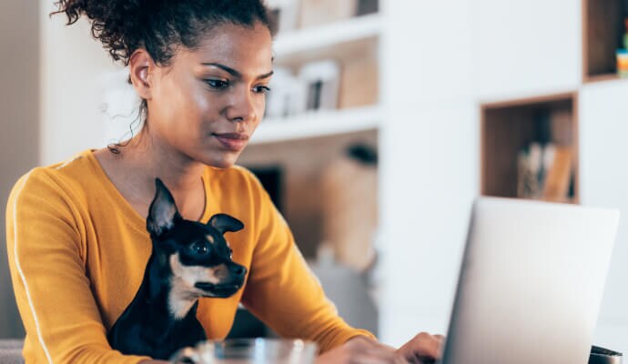 Nő laptopot használ, miközben kutya ül az ölében