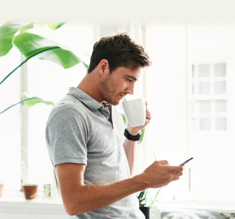 Férfi kávézik, miközben mobiltelefont tart a kezében