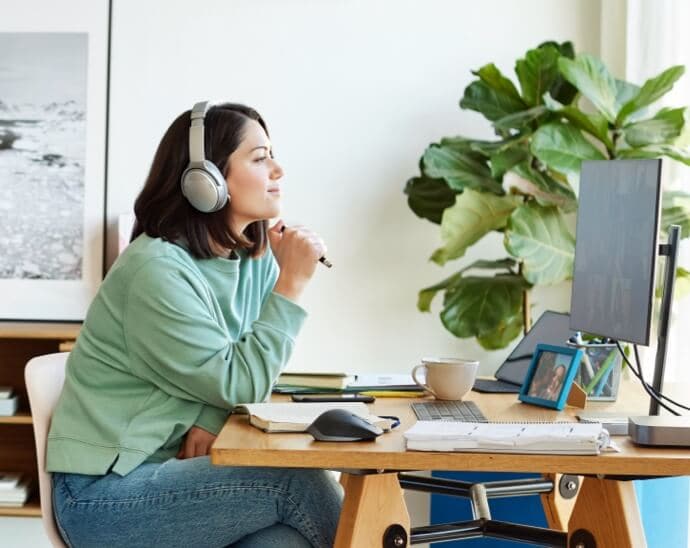 Fejhallgatót viselő, tollat tartó és egy PC monitorát néző nő