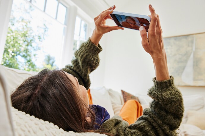 Fekvő nő egy mobiltelefonra néz